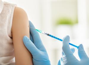 Close-up of young child's shoulder being injected with a vaccine by a gloved healthcare provider