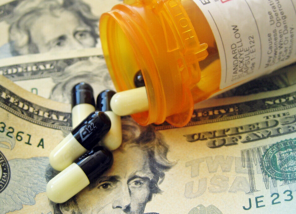Close-up of a bottle of prescription medication on its side with pills spilling out onto U.S. currency